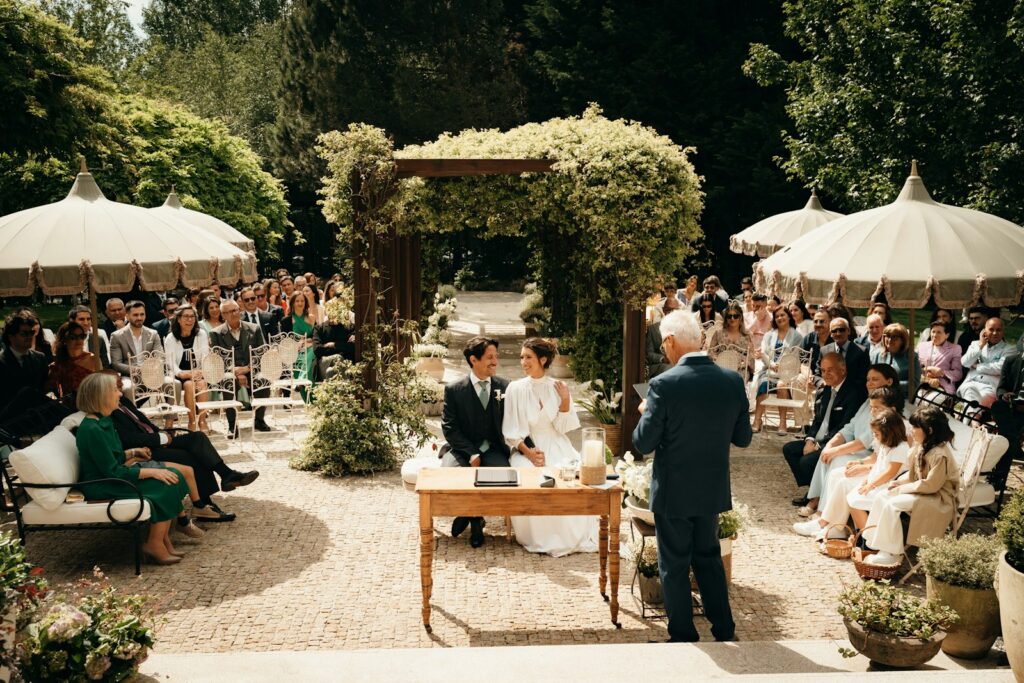 Mikrohochzeit im Freien: kleine Gästerunde sitzt bei der Trauung unter Sonnenschirmen