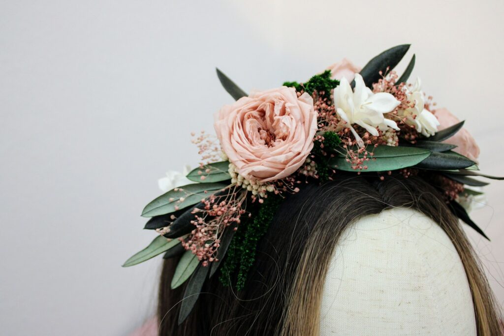 Blumenkranz mit rosa Rosen, weißen Blüten und grünen Blättern auf einer Büste