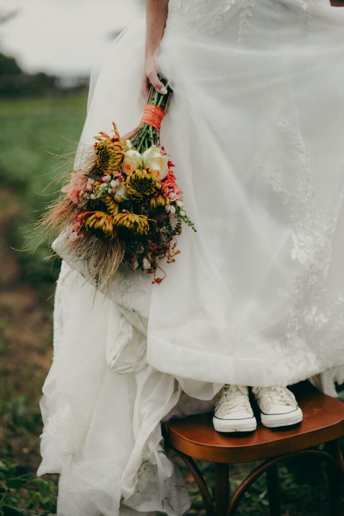 Braut im weißen Kleid mit buntem Brautstrauß trägt Sneaker