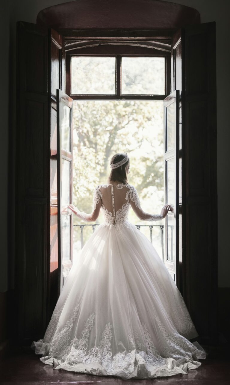 Braut im Spitzenkleid an einer offenen Balkontür