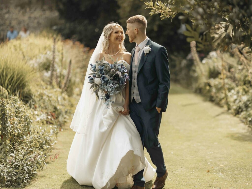 Brautpaar steht zwischen Bäumen und Sträuchern in einem Garten