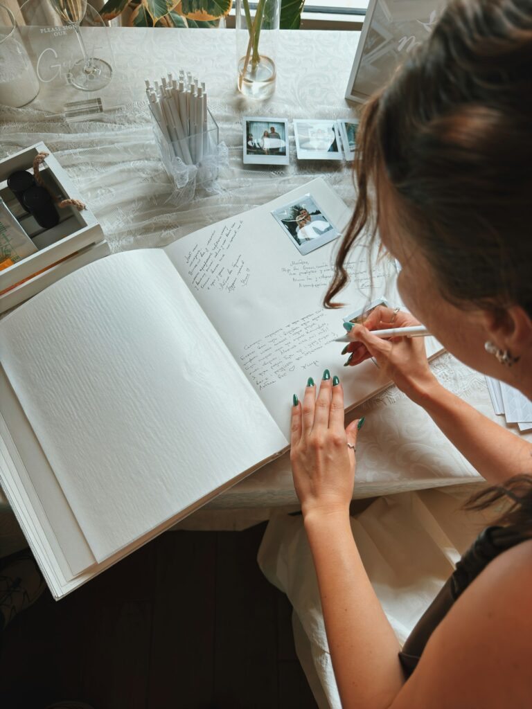 Frau schreibt mit weißem Stift Glückwünsche in ein Hochzeitsgästebuch