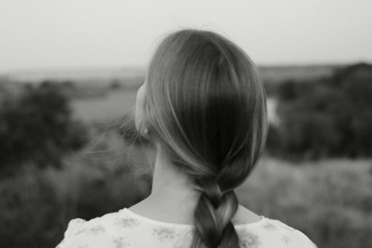 Frisur Hochzeitsgast einfach: Frau mit geflochtener Frisur von hinten vor unscharfer Landschaft