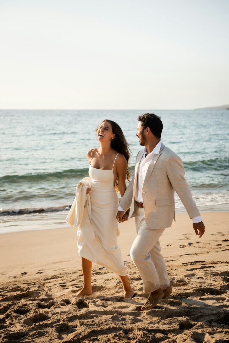 Heiraten im Ausland: frisch verheiratetes Paar läuft fröhlich am Strand entlang