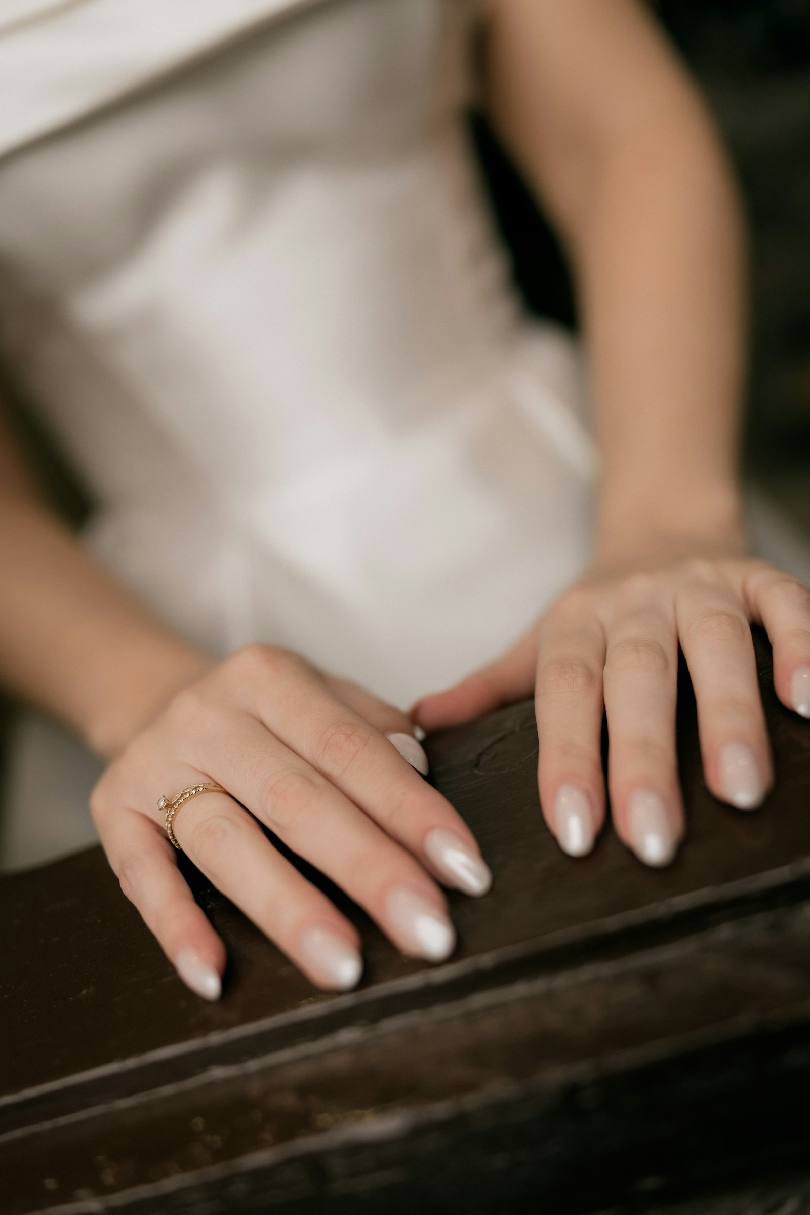 Hochzeitsnägel mit Perlglanz und Ring an eleganten Händen auf Holz