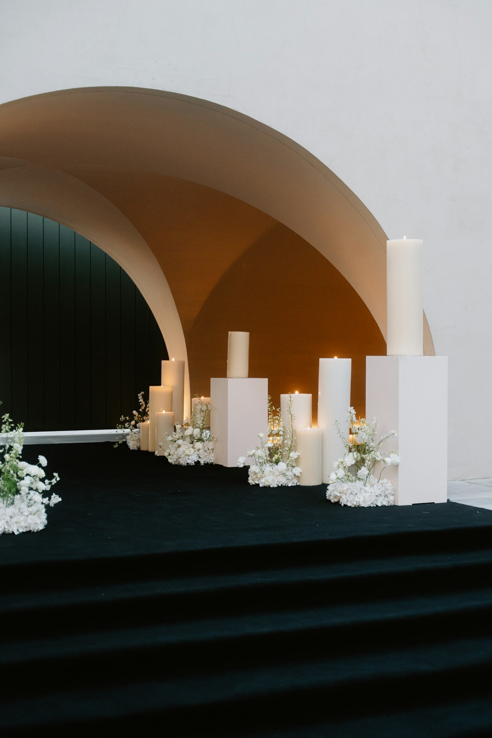 Weiße Kerzen auf Podesten mit schlichten Blumen