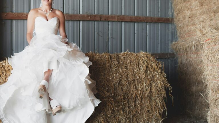 Braut im Rüschenkleid auf einem Strohballen in der Scheune